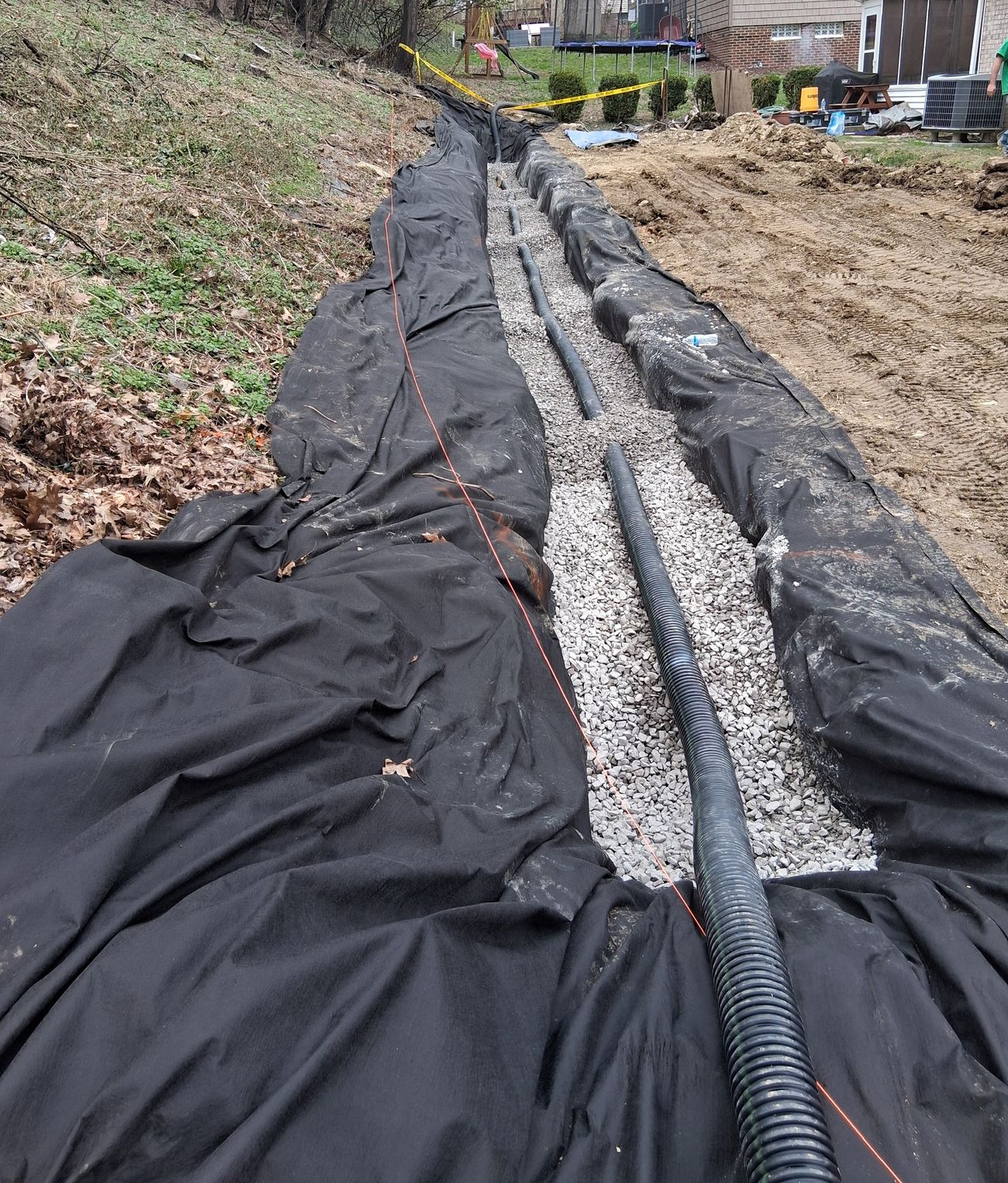 A French drain trench lined with fabric, with perforated pipe bedded in gravel