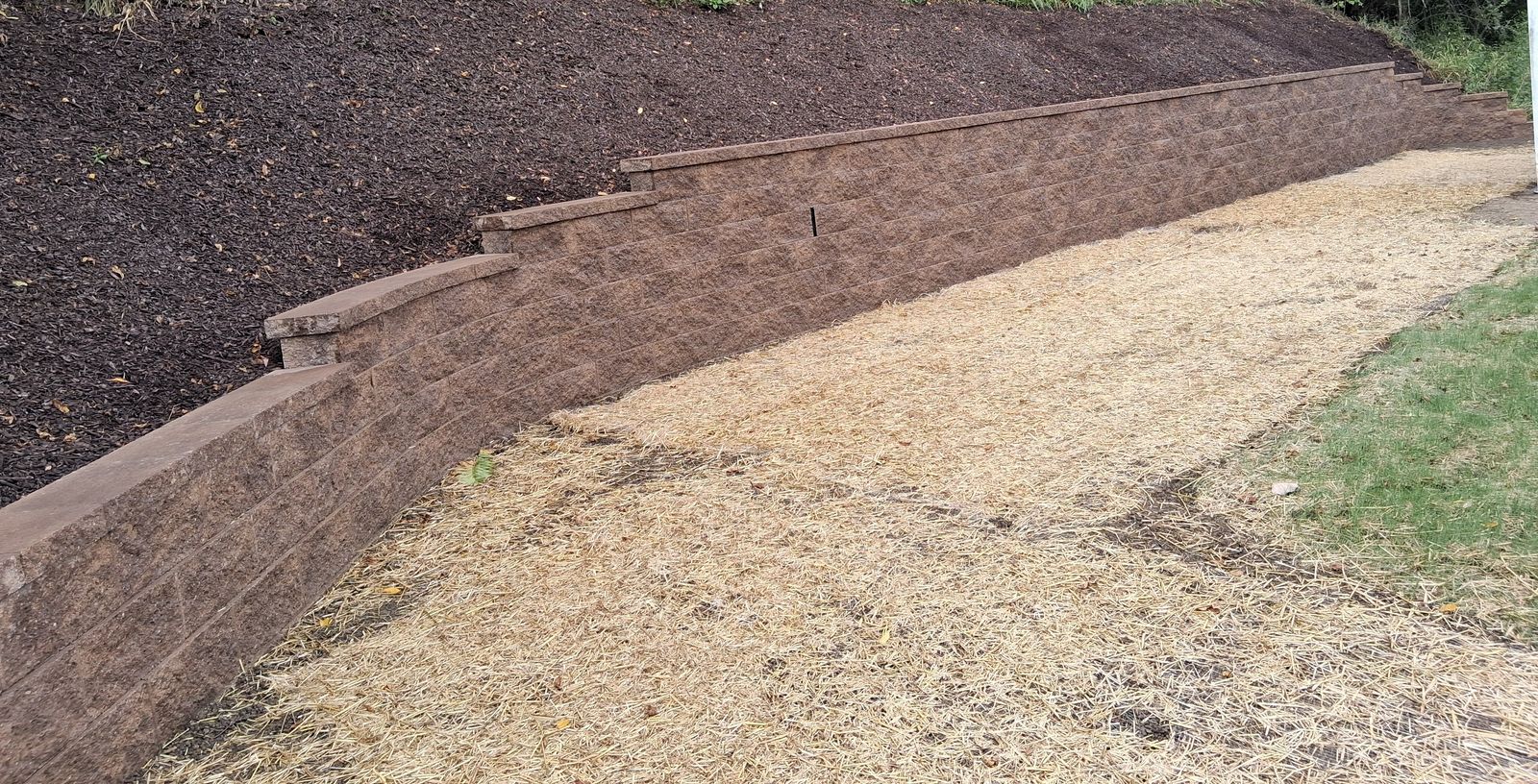 A long stepped block retaining wall holding back a mulched hillside