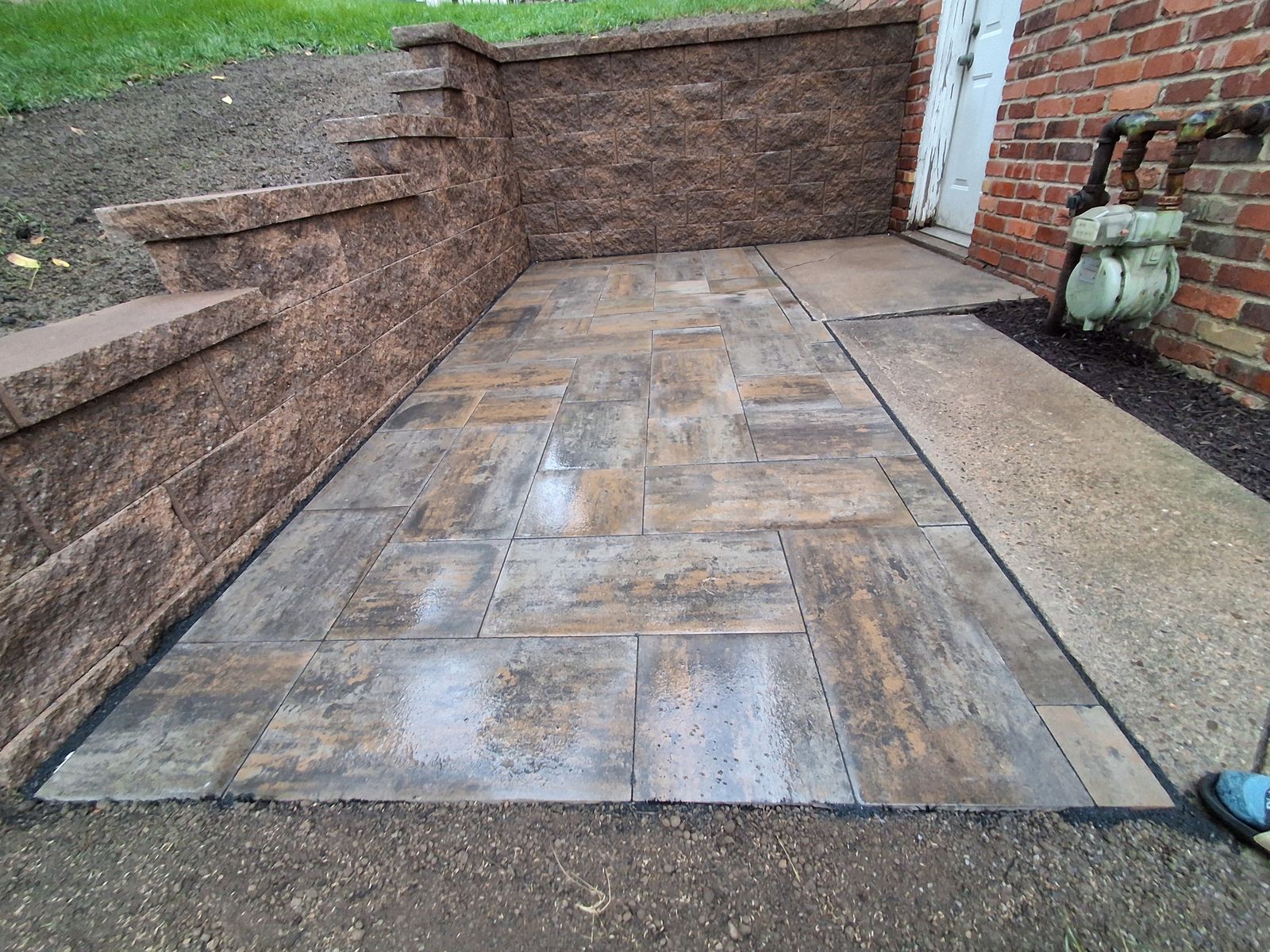 A new paver patio along a block retaining wall beside a brick house