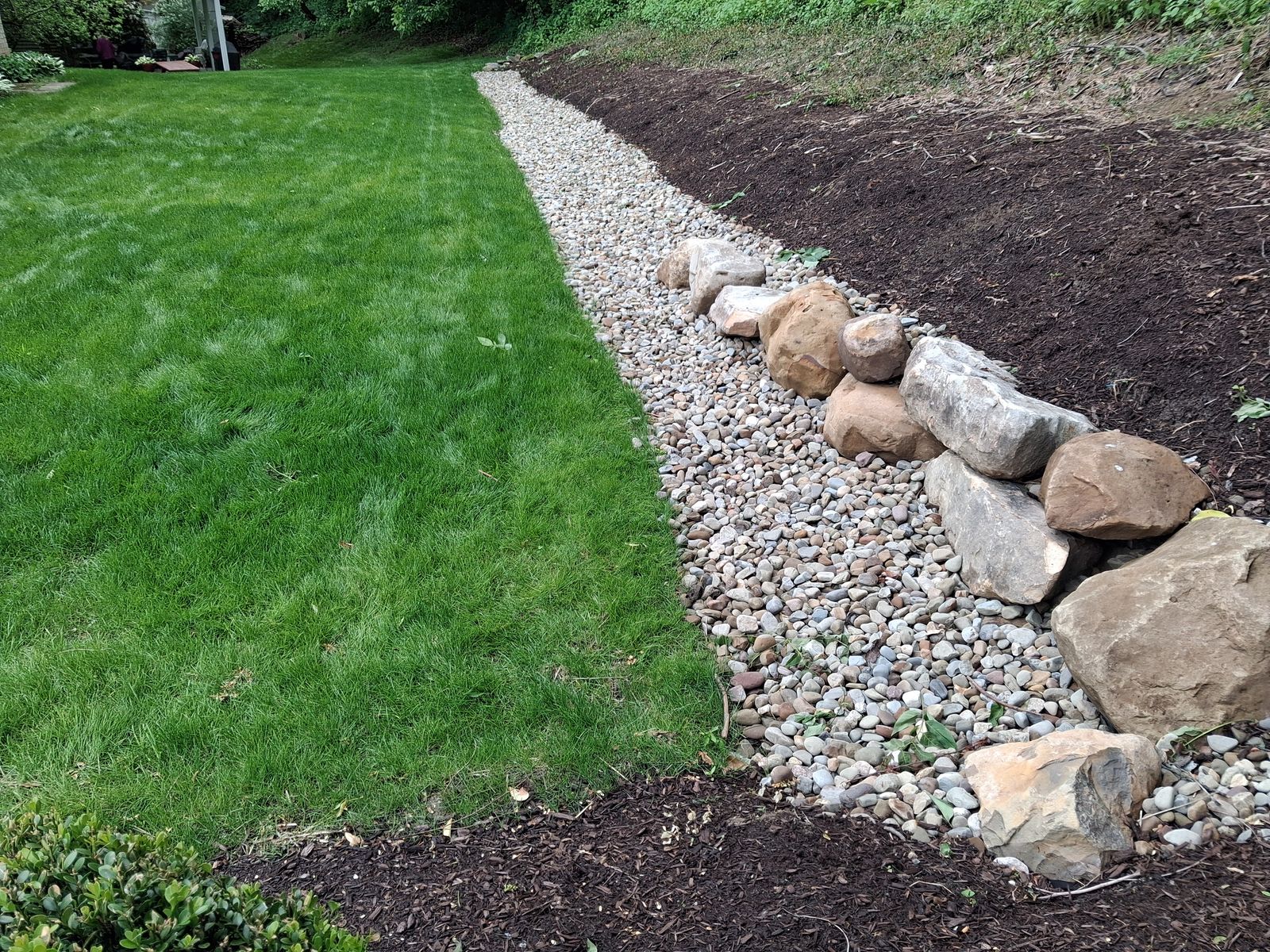 A river rock swale edged with boulders along a back yard slope